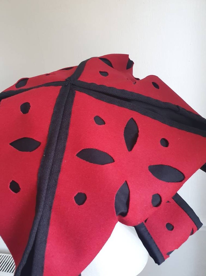 Puede incluir: Sombrero de fieltro rojo con dise&ntilde;os recortados en negro y ribete negro.