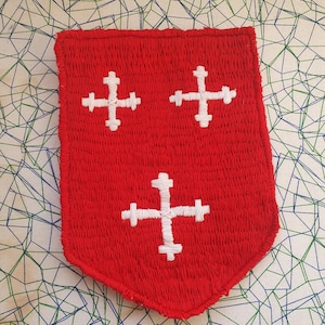 May include: Red fabric patch with three white embroidered crosses. The patch is shaped like a shield.
