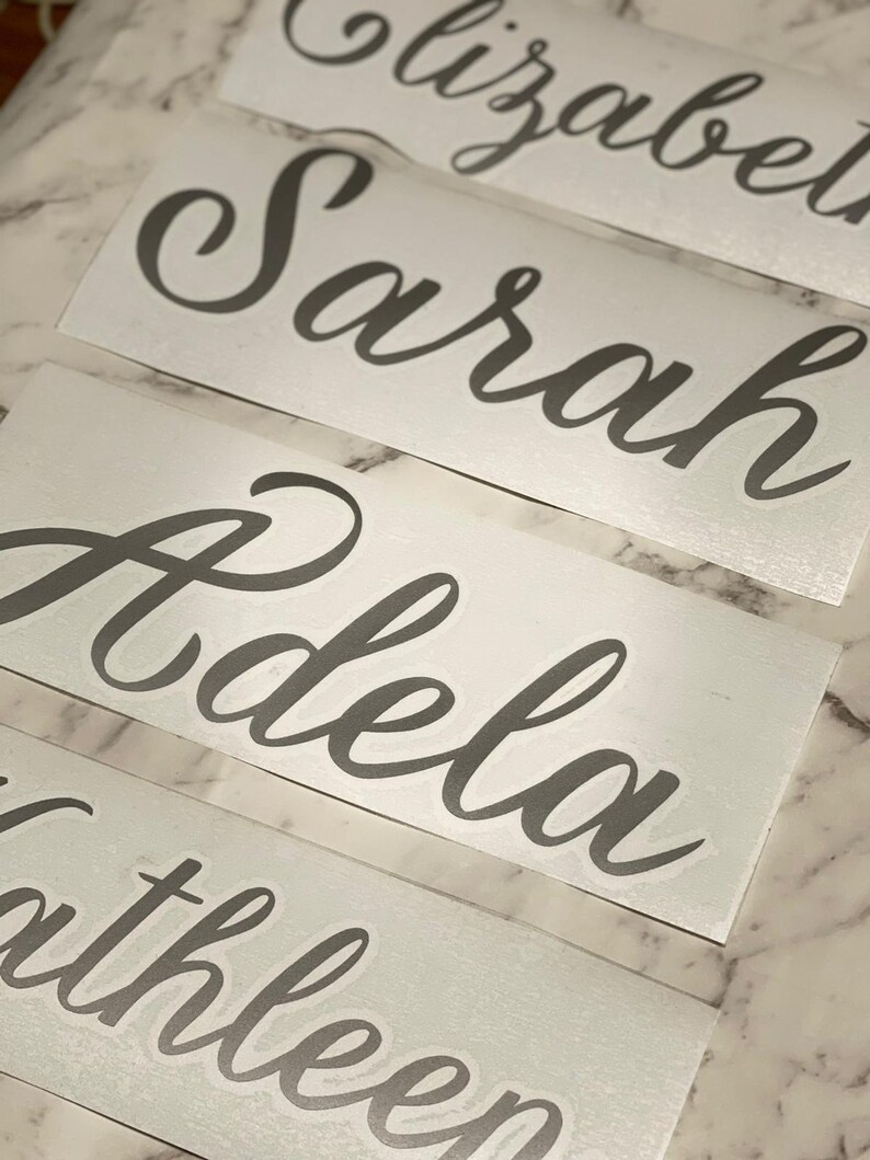 May include: Four white vinyl stickers with the names Elizabeth, Sarah, Adela, and Kathleen written in a cursive font.