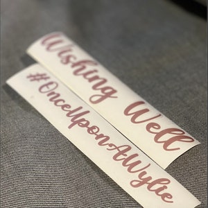 May include: Two white vinyl stickers with pink lettering. The top sticker says "Wishing Well" and the bottom sticker says "#OnceUponATime".