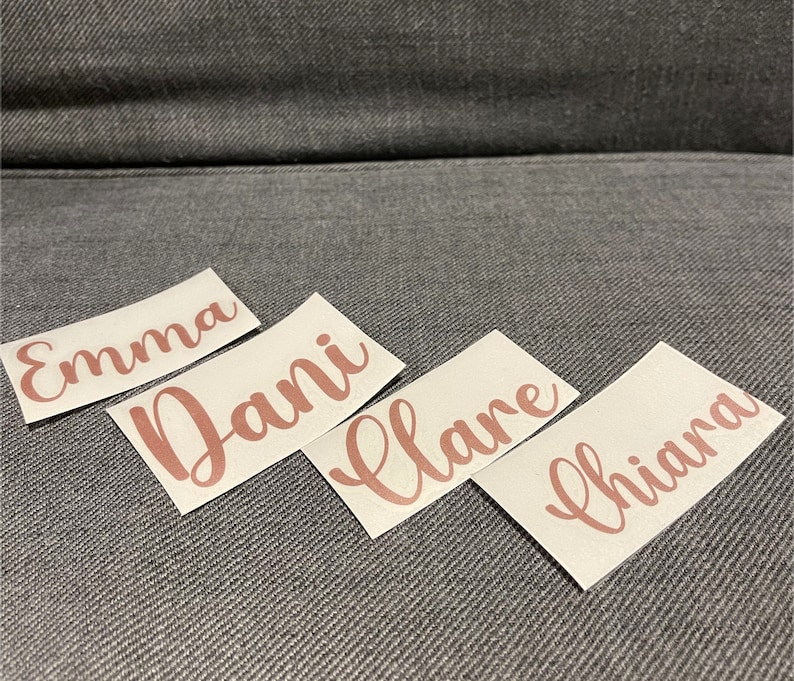 May include: Four white labels with the names Emma, Dani, Clare, and Chianna written in cursive script in a rose gold color.
