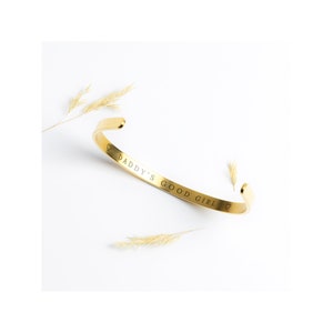 May include: Gold-toned bangle bracelet with the inscription "Daddy's Good Girl" and a heart symbol on either end.
