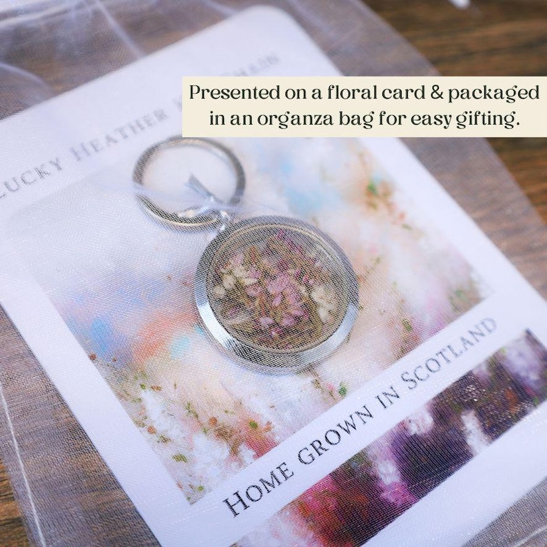 Pode incluir: Um porta-chaves prateado com um pendente redondo preenchido com flores rosa secas. O porta-chaves &eacute; apresentado num cart&atilde;o floral e embalado numa bolsa de organza. O texto "HOME GROWN IN SCOTLAND" &eacute; vis&iacute;vel.