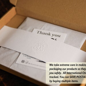 Pode incluir: Um close-up de um cart&atilde;o de agradecimento branco com uma pequena ilustra&ccedil;&atilde;o de um p&aacute;ssaro preto. O cart&atilde;o est&aacute; dentro de uma caixa de papel&atilde;o marrom com papel de seda branco. O texto "We take extreme care in making & packaging our products so they get to you safely. All International Orders are tracked. You can SAVE POSTAGE costs by buying multiple items." est&aacute; impresso no papel de seda.