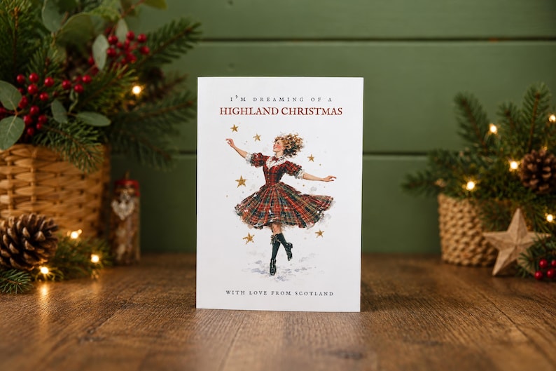 Pu&ograve; includere: Un biglietto d'auguri bianco con l'illustrazione di una persona che danza indossando un abito scozzese rosso e verde e stivali neri. Il testo recita I'M DREAMING OF A HIGHLAND CHRISTMAS e WITH LOVE FROM SCOTLAND, circondato da stelle dorate.