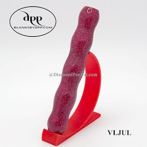 May include: A burgundy-colored pen with glitter, displayed on a red stand. The pen has a curved, ergonomic design. The stand is a bright red, with a curved shape. The text "VLJUL" is visible.