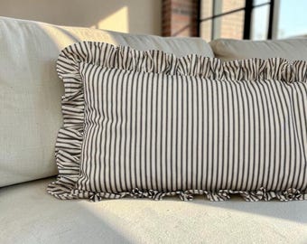 May include: A rectangular throw pillow featuring a vertical black and white pinstripe pattern. The pillow is finished with a gathered ruffle trim along all four edges, creating a textured border that frames the striped fabric design.