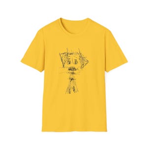 May include: Mustard yellow t-shirt featuring a black line drawing of a face. The artwork appears to be a simple, expressive sketch. The shirt has a classic crew neck and short sleeves.