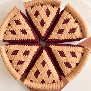 May include: Six felt pie slices arranged in a circle. Each slice features a tan crust and a lattice top over a burgundy filling. The pie slices are on a wooden surface.