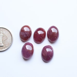 Puede incluir: Seis piedras preciosas ovaladas de color rojo con un ligero tono púrpura. Las piedras preciosas son lisas y pulidas.