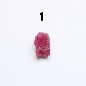 Puede incluir: Una gema de rub&iacute; en bruto, sin cortar, con un vibrante tono rojo rosado. La piedra natural tiene una forma irregular y una superficie texturizada. El n&uacute;mero "1" est&aacute; impreso encima de la gema.