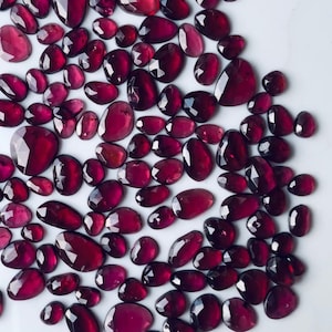 Puede incluir: Una colección de piedras preciosas rojas facetadas y sueltas. Las piedras preciosas son de varios tamaños y formas, con un acabado pulido y brillante.