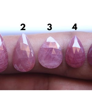 Peut inclure: Cinq pierres précieuses roses en forme de goutte d'eau, taillées à facettes, de tailles différentes. Numérotées de 1 à 5, elles sont présentées sur un fond neutre, mettant en valeur leur couleur et leur taille.