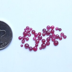 以下が含まれることがあります： 白い表面に散らばった、丸いものとわずかに楕円形のものがあるルビーレッドの宝石のコレクション。宝石はさまざまなサイズです。