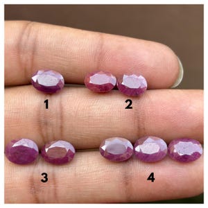 May include: Seven oval-cut, faceted pinkish-red gemstones arranged in four numbered groups. The stones exhibit a translucent quality with visible internal inclusions and are displayed against a skin-toned background for scale and color reference.