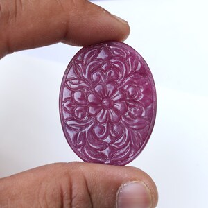 May include: A carved oval ruby gemstone with a floral design. The ruby is a deep pink colour and has a high polish.