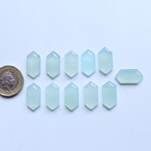 May include: Twelve light blue, faceted, hexagonal cabochon gemstones. The stones are arranged in two rows of six, with the top row slightly offset from the bottom row.