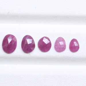 Puede incluir: Cinco gemas facetadas de forma ovalada, dispuestas en fila. Las gemas varían en tamaño y muestran tonos de rosa y magenta. Las piedras tienen una superficie pulida, listas para ser engarzadas. Medidas en centímetros.