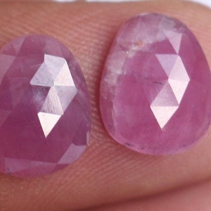 Puede incluir: Dos piedras preciosas rosadas facetadas con un corte de rosa. Las piedras preciosas son de forma ovalada y tienen un acabado brillante y pulido.