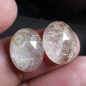 以下が含まれることがあります： 金色のインクルージョンが入った、透明な楕円形の水晶が2つ。石はファセットカットされており、半透明な外観をしています。