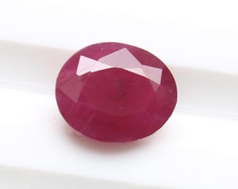 May include: A faceted, oval-shaped ruby gemstone. The gem is a deep, rich red color with multiple reflective facets. The ruby is set against a white background, highlighting its color and clarity. This gemstone is suitable for jewelry.