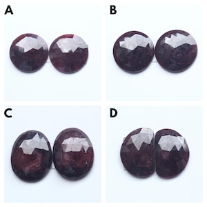 May include: Four pairs of dark purple gemstones, each pair is arranged side-by-side. The gemstones are faceted and have a round or oval shape. The gemstones are labelled A, B, C, and D.