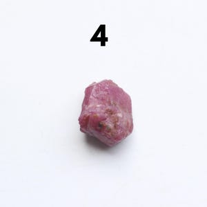 Puede incluir: Una gema de rub&iacute; rosa rugosa con forma irregular. El n&uacute;mero "4" est&aacute; impreso en negro encima de la gema. El rub&iacute; tiene una superficie texturizada y diferentes tonos de rosa.
