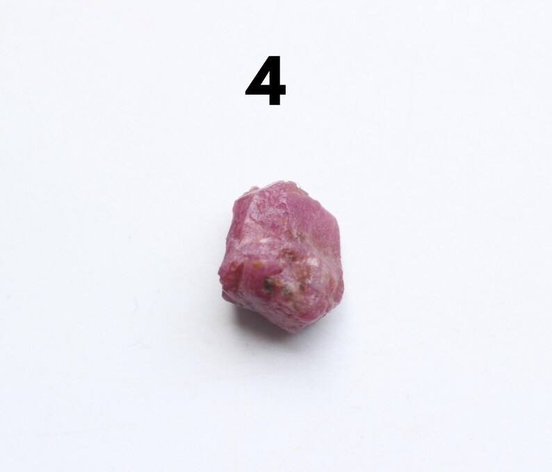 Puede incluir: Una gema de rub&iacute; rosa rugosa con forma irregular. El n&uacute;mero "4" est&aacute; impreso en negro encima de la gema. El rub&iacute; tiene una superficie texturizada y diferentes tonos de rosa.