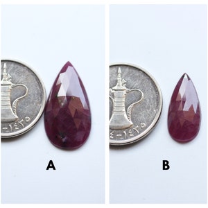 May include: Two pear-shaped faceted gemstones, one larger than the other, both a deep reddish-purple color. The gemstones are shown next to a coin for size comparison. The larger gemstone is labeled "A" and the smaller gemstone is labeled "B".