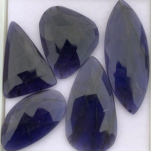 Peut inclure: Cinq pierres précieuses facettées de couleur violette avec une teinte foncée, presque noire. Les pierres sont taillées dans différentes formes, notamment ovale, goutte d'eau et triangulaire.