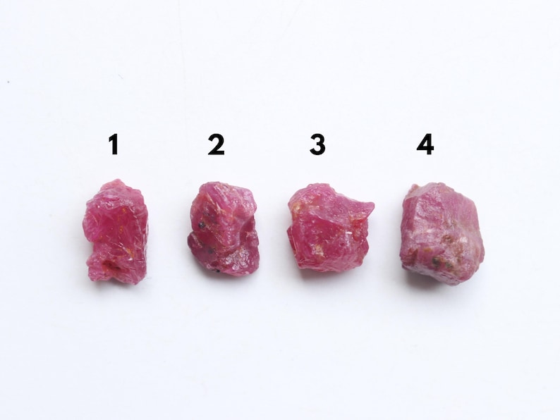 Puede incluir: Cuatro piedras preciosas de rub&iacute; en bruto y sin cortar se muestran sobre un fondo blanco. Las piedras preciosas est&aacute;n numeradas del 1 al 4. Cada rub&iacute; tiene un color rojo rosado intenso y una textura rugosa e irregular.