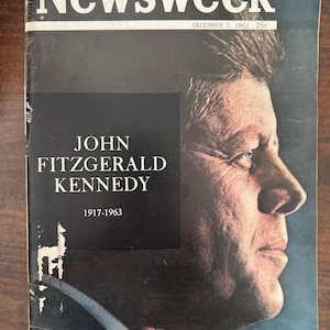 May include: A vintage Newsweek magazine cover featuring a profile of John F. Kennedy. The cover has the title "Newsweek" in white letters at the top, with the date December 2, 1963, and the price 25c. The magazine cover has a black rectangle with the name "JOHN FITZGERALD KENNEDY" and the years "1917-1963".