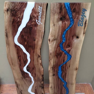 May include: Two wooden cutting boards with a white and blue epoxy resin river design. The boards are personalized with the names "Gormet" and "Blarzey".