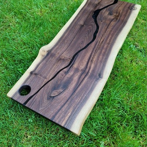 May include: A large wooden serving board with a live edge and a black epoxy river running through the center. The board has a hole on the side for hanging.