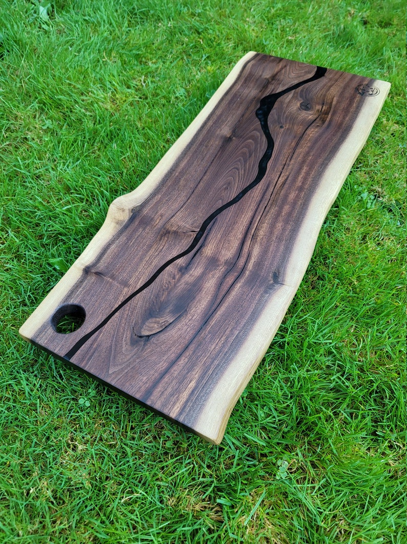 May include: A large wooden serving board with a live edge and a black epoxy river running through the center. The board has a hole on the side for hanging.