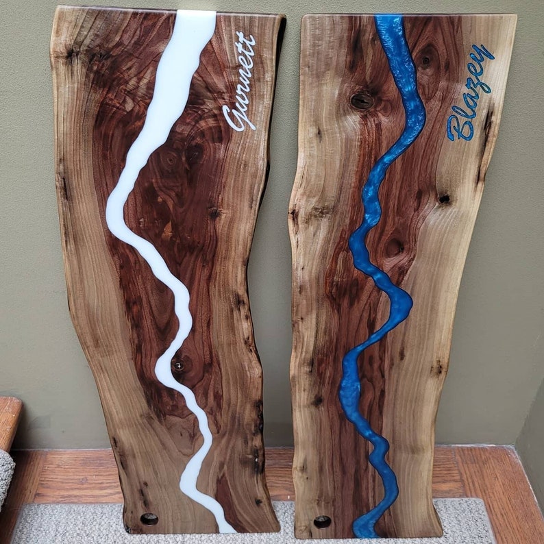 May include: Two wooden cutting boards with a white and blue epoxy resin river design. The boards are personalized with the names "Gormet" and "Blarzey".