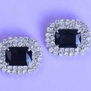 Puede incluir: Un par de hebillas de zapatos plateadas con piedras de imitación rectangulares negras rodeadas de piedras de imitación transparentes.