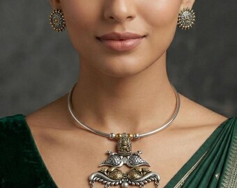 Puede incluir: Una mujer que lleva un collar de plata con un colgante detallado y pendientes a juego. El colgante presenta elementos dorados y plateados con detalles colgantes. Lleva un top de terciopelo verde oscuro y un sari verde con ribete dorado.