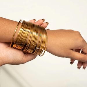 May include: A stack of gold-colored metal bangles worn on a person's wrist.