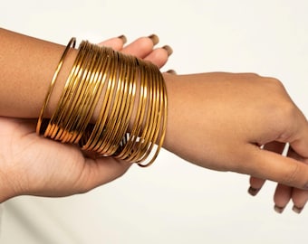 May include: A stack of gold-colored metal bangles worn on a person's wrist.