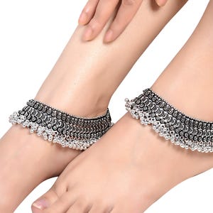 May include: A pair of silver anklets with intricate designs and dangling beads. The anklets are worn on a person's ankles.