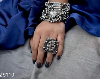 May include: A large silver ring with a round design and multiple small beads. The ring is worn on a finger with dark nail polish.