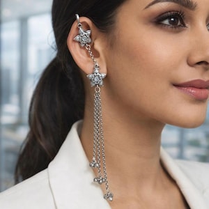 May include: A silver ear cuff and earring set. The ear cuff has a star-shaped design with a central gem and a chain that connects to a dangling earring. The earring has a star-shaped design with a central gem and multiple chains with small bell-shaped charms.