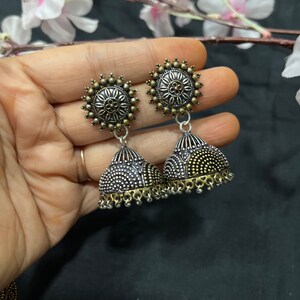 Op de afbeelding: Een paar zilveren en gouden oorhangers met een bloemmotief. De oorhangers hebben een ronde bovenkant en een klokvormige onderkant.