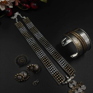 May include: An assortment of silver and gold-toned jewelry on a black surface. The set includes a necklace, earrings, a ring, a bracelet, and a pendant. The necklace features a beaded design, and the bracelet has an engraved floral pattern.
