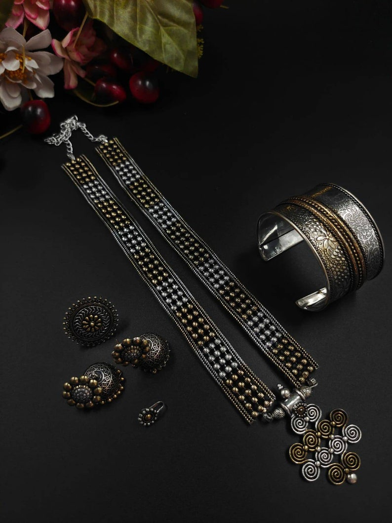 May include: An assortment of silver and gold-toned jewelry on a black surface. The set includes a necklace, earrings, a ring, a bracelet, and a pendant. The necklace features a beaded design, and the bracelet has an engraved floral pattern.