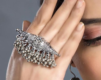 May include: Silver-toned statement ring featuring intricate geometric patterns and dangling bead accents. The ring's design includes a central, textured element with a series of hanging, small, round beads. This bold piece of jewelry adds a touch of bohemian flair.