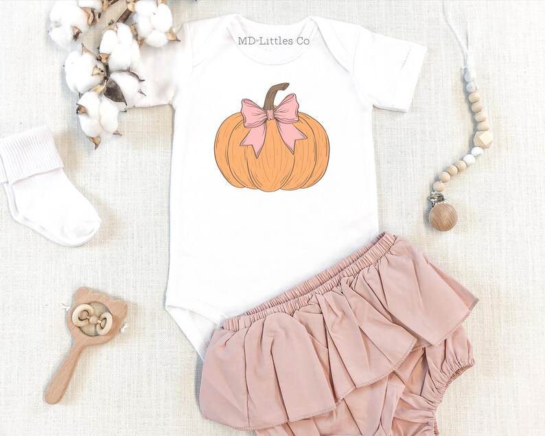 White onesie with a design that features a drawn pumpkin with a pink bow tied on the stem.