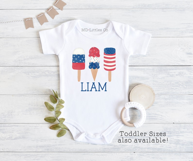 K&ouml;nnte beinhalten: Ein wei&szlig;er Baby-Strampler mit einem roten, wei&szlig;en und blauen Eiswaffel- und Eis am Stiel-Design. Der Strampler tr&auml;gt den Namen "LIAM" aufgedruckt. Der Text "Kleinkindgr&ouml;&szlig;en ebenfalls erh&auml;ltlich!" ist unter dem Strampler aufgedruckt.
