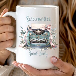 May include: White ceramic mug featuring a teal vintage typewriter design with floral accents and a pink bow. The mug has the text "Screenwriter" and "Sarah Lively" in a light blue script. A perfect gift for writers.